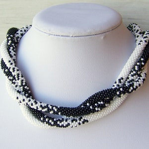 May include: A black and white beaded necklace with a twisted design. The necklace is made of small, round beads and is approximately 18 inches long.