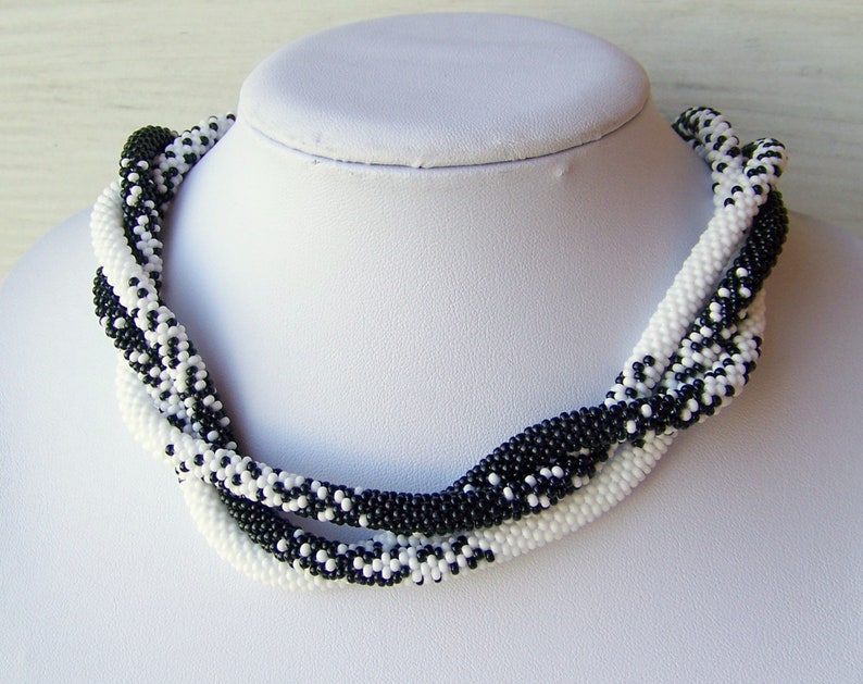 May include: A black and white beaded necklace with a twisted design. The necklace is made of small, round beads and is approximately 18 inches long.