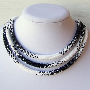 May include: A black and white beaded necklace with a multi-strand design. The necklace is made of small, round beads that are woven together in a pattern.