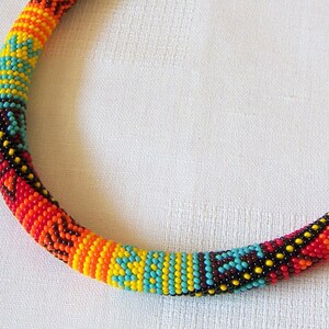 May include: A colorful beaded necklace with a geometric pattern in shades of red, orange, yellow, blue, and black.