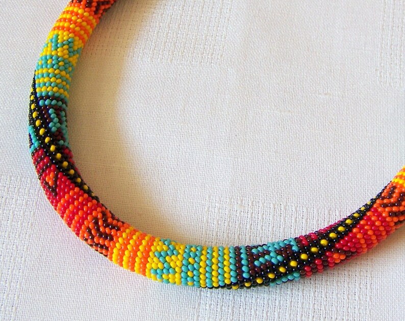 May include: A colorful beaded necklace with a geometric pattern in shades of red, orange, yellow, blue, and black.