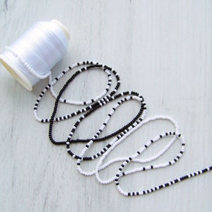 May include: A spool of white thread and two strands of black and white beads.