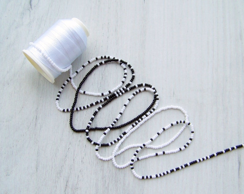 May include: A spool of white thread and two strands of black and white beads.