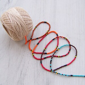 May include: A ball of beige yarn and a long strand of colorful beads in red, orange, black, brown, and blue.