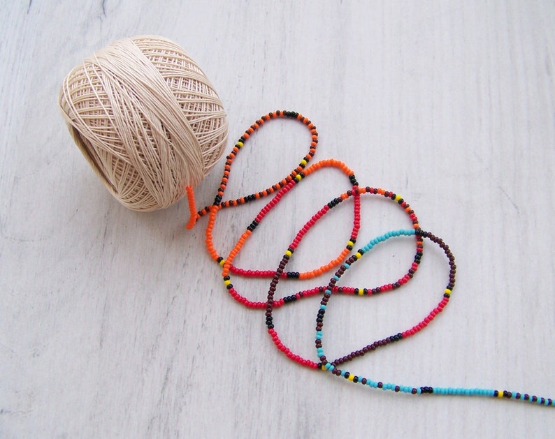 May include: A ball of beige yarn and a long strand of colorful beads in red, orange, black, brown, and blue.