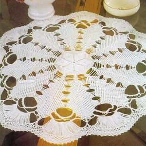 May include: White crocheted table runner with a delicate floral design. The runner features a central motif with a repeating pattern of flowers and leaves.
