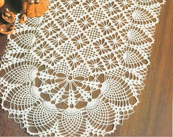 Könnte beinhalten: Ein weißer gehäkelter Tischläufer mit einem zarten Blumenmuster. Der Läufer liegt auf einem Holztisch mit Dekorationsartikeln.