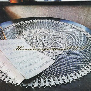 May include: A white, intricately crocheted doily with a floral center design. The doily is placed on a dark surface, with sheet music and a violin in the background. The text "Homedecorpattern P.D.F" is visible on the sheet music.