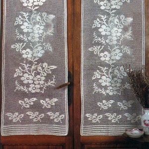 Puede incluir: Dos cortinas blancas de ganchillo con diseños florales cuelgan de una puerta de madera con detalles tallados. Las cortinas están hechas de encaje delicado y presentan un patrón repetitivo de flores y hojas.