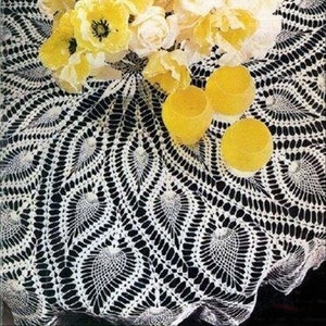 May include: A white crocheted tablecloth with a black and white peacock feather design. The tablecloth is round and has a scalloped edge. There are four yellow glass cups on the tablecloth.