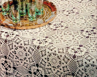 May include: A white crocheted tablecloth with a delicate floral pattern. A green glass bottle with a silver stopper and a tray of shot glasses are on the table.