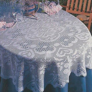 May include: A white crocheted tablecloth with a delicate floral pattern, laid out on a blue table with a wooden chair in the background.