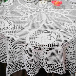 May include: White crocheted tablecloth with a delicate floral pattern. The tablecloth is laid on a round table with a teapot, teacups, and a bowl of candy.