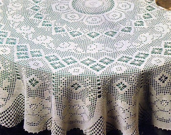 May include: A white crocheted tablecloth with a delicate floral pattern, featuring a green center circle and a scalloped edge. The tablecloth is laid on a round table with a green surface.