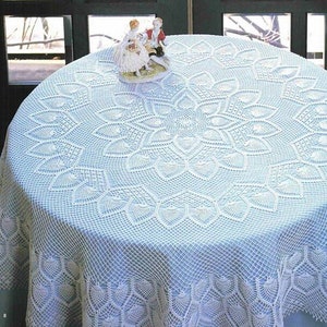 May include: A white crocheted tablecloth with a delicate floral pattern. The tablecloth is laid on a light blue table and features a small porcelain figurine in the centre.