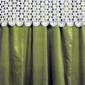 Puede incluir: Una cortina de color verde oliva con un borde de encaje de ganchillo blanco en la parte superior con un acabado festoneado. En la esquina inferior izquierda, se ve parte de un recipiente de cerámica blanco con un patrón floral negro.