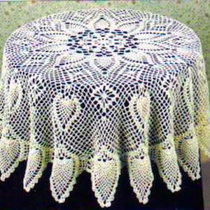 May include: A white crocheted tablecloth with a delicate floral pattern and scalloped edges. The tablecloth is made with a fine yarn and has a delicate, lacy appearance.