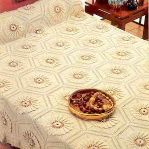 Puede incluir: Una colcha de ganchillo blanca con un patrón repetitivo de grandes flores caladas. La colcha está colocada sobre una cama con una cabecera de madera y una mesita de noche de madera marrón.