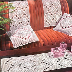Puede incluir: Cojines y un camino de mesa de ganchillo blanco con un patrón de diamante y detalles florales sobre un sofá de terciopelo rojo y una mesa de café.