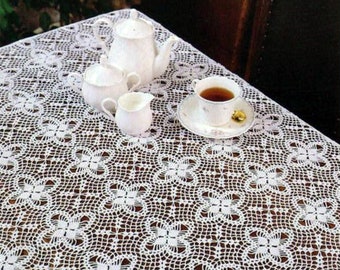 May include: White crocheted tablecloth with a delicate floral pattern. The tablecloth is laid on a wooden table with a teacup and saucer, a teapot, and two creamer containers.