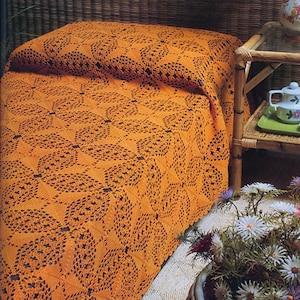 May include: A bright orange crochet bedspread featuring a repeating geometric floral pattern with intricate openwork details. The textile is draped over a surface, showcasing the textured, knotted yarn construction and the consistent, symmetrical design.