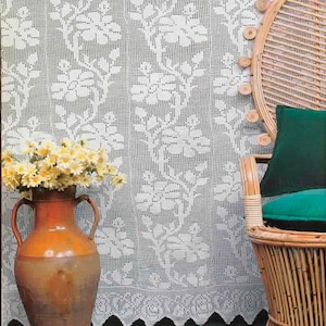 May include: A white lace curtain with a floral pattern hangs behind a wicker chair with a green cushion. A brown and orange ceramic vase holds yellow flowers. The scene is set against a teal-colored surface.
