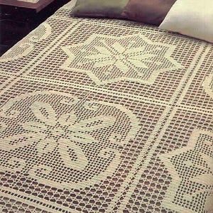 May include: A cream-colored, open-weave crochet bedspread with a geometric star and floral pattern. The bedspread is draped over a bed with pillows in shades of green, brown, and white. The crochet design features intricate details and a textured appearance.