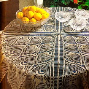 May include: A crocheted table cloth with a delicate, intricate design. The cloth is beige and features a repeating pattern of leaves. The cloth is laid out on a table with a bowl of lemons and three glass bowls.