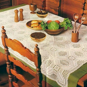May include: A dining table set for a meal, featuring a white lace tablecloth with a green border. Wooden bowls, salt and pepper shakers, and serving spoons are arranged on the table, along with bread and vegetables.