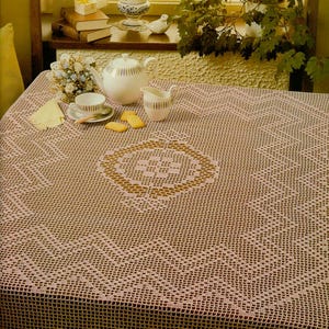 May include: A rectangular tablecloth featuring a light pink crochet pattern with a central geometric motif and a zigzag border design. The fabric has an open-work grid structure throughout, creating a delicate and intricate texture across the surface.
