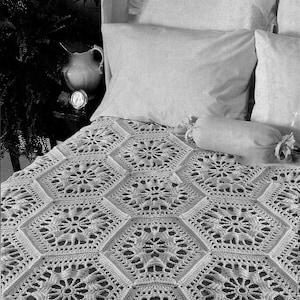 Puede incluir: Una manta blanca de ganchillo con un patrón floral hexagonal cubre una cama. La cama tiene almohadas blancas y un cojín cilíndrico. El intrincado diseño de la manta es visible, mostrando la detallada artesanía. La estética general es suave y acogedora.