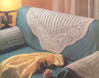 May include: A white crocheted sofa throw with a floral design. The throw is draped over a teal sofa with a white crocheted pillow and a yellow throw pillow.