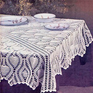 May include: White crocheted tablecloth with a delicate lace pattern. The tablecloth is laid out on a table with two plates and a bowl.