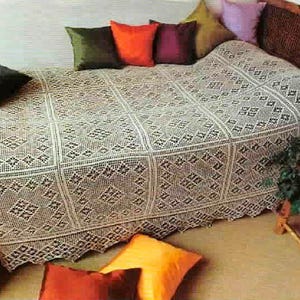 May include: A cream-colored crocheted bedspread featuring a repeating square pattern with intricate geometric diamond motifs. The bedspread is draped over a bed and is accented by several solid-colored throw pillows in shades of orange, purple, green, and yellow.
