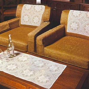 Peut inclure: Deux fauteuils dorés avec des napperons blancs à motifs d'étoiles sur le dossier. Un napperon blanc assorti est sur une table basse en bois foncé, avec une bouteille et des verres. Les fauteuils ont un revêtement à motifs.