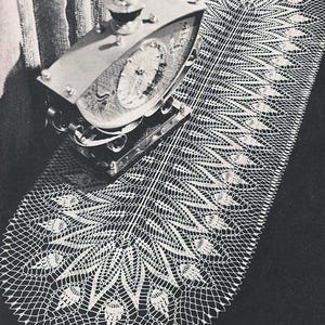 Puede incluir: Imagen en blanco y negro de un camino de mesa de encaje blanco tejido a ganchillo con un diseño de plumas de pavo real. Un reloj plateado descansa sobre el camino de mesa. El diseño es simétrico y detallado.