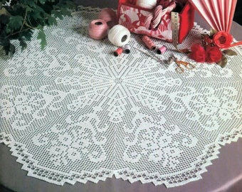 May include: White crocheted table cloth with a delicate floral pattern. The tablecloth is laid on a round table with a gray surface. There are various sewing supplies on the table, including spools of thread, scissors, and a small box with a red lid.
