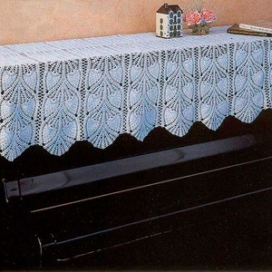May include: White crocheted piano scarf with a scalloped edge. The scarf is draped over a black piano.