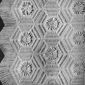 Puede incluir: Una manta de ganchillo de color blanquecino con un patrón hexagonal repetido. Cada hexágono presenta un motivo floral central. La manta está rematada con un borde con flecos, que añade un toque decorativo al textil hecho a mano. Mide aproximadamente 150 cm x 200 cm.