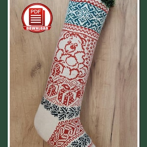 May include: A knitted Christmas stocking with a festive design. The stocking features a pattern of red teddy bears, gifts, and snowflakes on a white background, with teal and white geometric patterns at the top. The text "CHRISTMAS STOCKING | CHRISTMAS TEDDY BEAR PDF KNITTING PATTERN # A29" is at the top.
