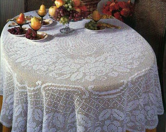 Puede incluir: Un mantel de crochet blanco con un delicado patrón floral cubre una mesa redonda. La mesa está puesta con fruta y flores, creando un centro de mesa encantador y elegante.