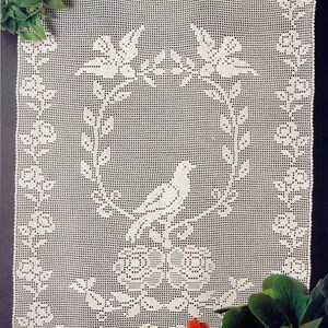 以下が含まれることがあります： 鳥と花のデザインが施された白いクロシェのドイリー。ドイリーは繊細な透かし模様でできています。