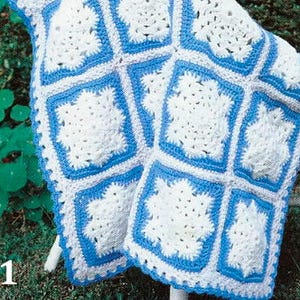 Könnte beinhalten: Eine handgefertigte Häkeldecke mit einem wiederkehrenden Muster aus weißen quadratischen Motiven mit strukturierten Zentren, die jeweils von einem leuchtend blauen Garnrahmen umgeben sind. Die Decke besteht aus mehreren verbundenen Quadraten und enthält den weißen Text #1.