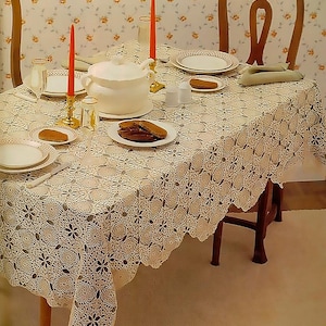 Può includere: Un tavolo da pranzo apparecchiato per un pasto, con una tovaglia all'uncinetto color crema con un motivo floreale. Il tavolo è apparecchiato con piatti bianchi, una zuppiera e candele rosse in candelabri dorati. Lo sfondo ha una carta da parati floreale.