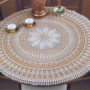 Puede incluir: Mantel de mesa de crochet blanco con un delicado dise&ntilde;o floral en el centro. El mantel est&aacute; puesto sobre una mesa de madera con dos tazas de t&eacute; blancas y un taz&oacute;n peque&ntilde;o.