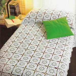 May include: A white crocheted bedspread featuring a repeating geometric pattern of circular motifs and small diamond-shaped cutouts, draped over a bed. A solid bright green square throw pillow rests on top of the white crocheted bedspread.