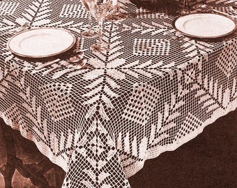 Può includere: Una tovaglia bianca, finemente lavorata all'uncinetto, con un motivo geometrico a fiocco di neve. La tavola è apparecchiata per una cena formale, con piatti, posate e bicchieri. Un centrotavola floreale e candele completano l'elegante allestimento.