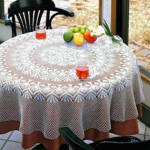 May include: White crocheted tablecloth with a delicate floral pattern, laid over a brown table with two glasses of red liquid and a plate of fruit.