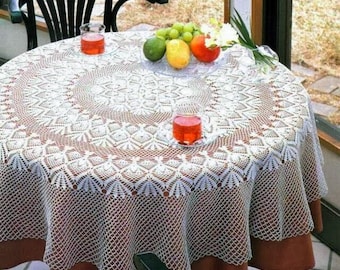 Puede incluir: Mantel de mesa de crochet blanco con un delicado patrón floral, colocado sobre una mesa marrón con dos vasos de líquido rojo y un plato de fruta.