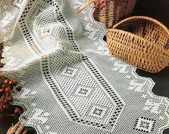 May include: White crocheted table runner with a delicate floral pattern. The runner is laid out on a dark surface with wicker baskets and wheat stalks.